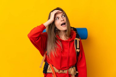 Sarı arka planda izole edilmiş büyük sırt çantalı Slovak dağcı kadın yan tarafa bakarken sürpriz jest yapıyor.
