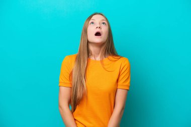 Genç Rus kadın mavi arka planda izole edilmiş yukarı bakıyor ve şaşırmış bir ifadeyle