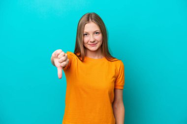 Mavi arka planda izole edilmiş genç bir Rus kadın başparmağının olumsuz ifadesini gösteriyor.