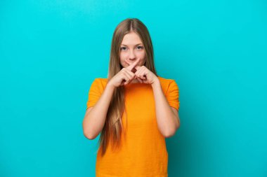 Mavi arka planda izole edilmiş genç bir Rus kadın sessizlik işareti gösteriyor.