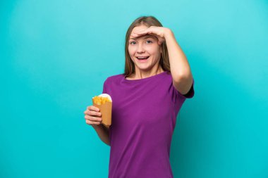 Mavi arka planda izole edilmiş patates kızartması yiyen genç Rus kadın yan tarafa bakarken sürpriz jest yapıyor.