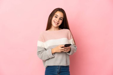 Pembe arka planda izole edilmiş küçük bir kız cep telefonuyla mesaj gönderiyor.