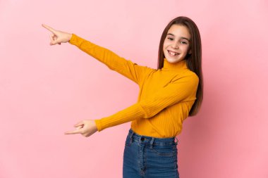 Pembe arka planda izole edilmiş küçük bir kız parmağıyla yan tarafı gösteriyor ve bir ürün sunuyor.