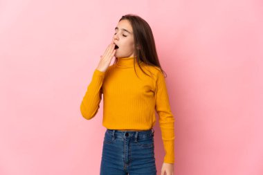 Pembe arka planda izole edilmiş küçük bir kız esniyor ve elleriyle ağzını kapatıyor.