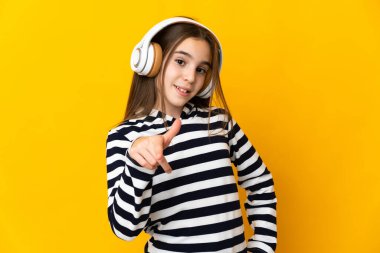 Sarı arka planda izole edilmiş küçük kız müzik dinliyor.
