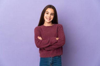 Mor arka planda izole edilmiş küçük bir kız kollarını ön tarafta çapraz tutuyor.
