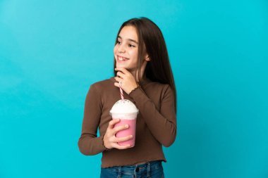 Mavi arka planda izole edilmiş çilekli milkshake 'i olan küçük kız yana bakıyor ve gülümsüyor.