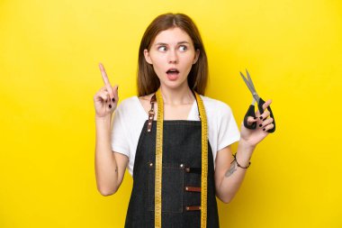 Genç terzi kadın, sarı arka planda izole edilmiş bir şekilde parmağını kaldıran bir fikir düşünüyor.