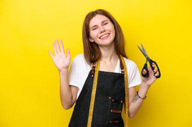 Genç terzi, sarı arka planda izole edilmiş mutlu bir ifadeyle selamlaşan İngiliz kadın.