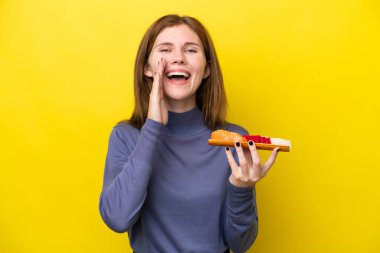 Sarı arka planda saşimi tutan genç İngiliz kadın ağzı açık bağırıyor.
