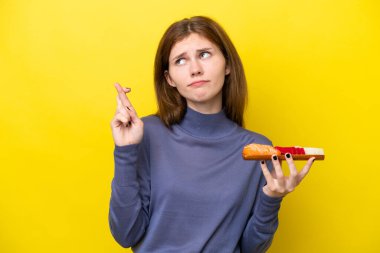 Sarı arka planda saşimi tutan genç İngiliz kadın parmaklarını çapraz yapıp en iyisini diliyor.