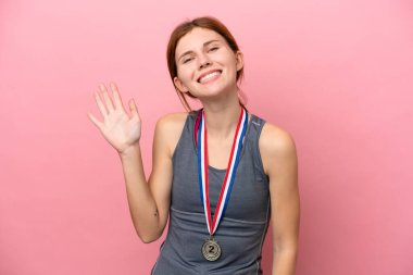 Pembe arka planda madalyalı genç bir İngiliz kadını mutlu bir ifadeyle selamlıyor.