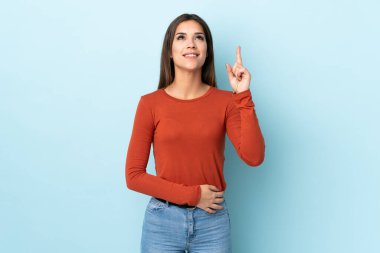 Mavi arka planda izole edilmiş genç beyaz kadın yukarı bakıyor ve şaşırıyor.