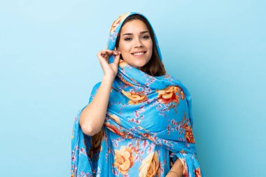 Geleneksel kostümlü genç Faslı kadın mavi arka planda izole edilmiş gülüyor.