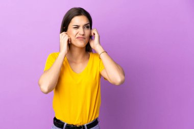 İzole edilmiş arka planda genç beyaz kadın hayal kırıklığına uğramış ve kulaklarını kapatmış.