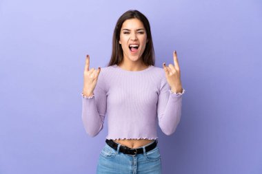 Tecrit edilmiş arka planda genç beyaz bir kadın boynuz hareketi yapıyor.