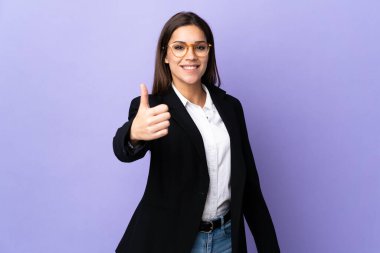 Mor arka planda izole edilmiş bir iş kadını. Başparmakları havada. Çünkü iyi bir şey oldu.