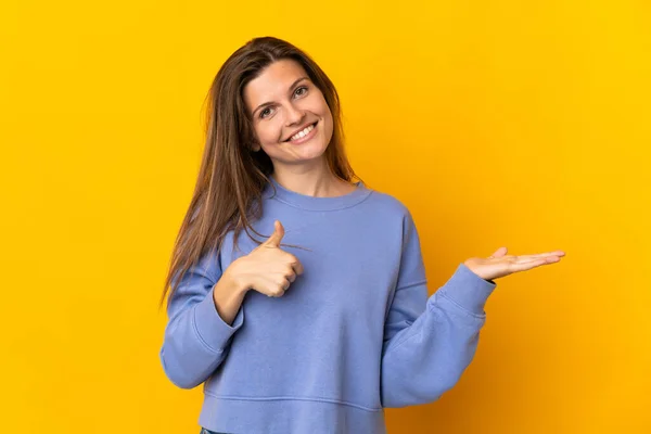 年轻的斯洛伐克女人 背景是黄色的 手掌上有一个想象的复制空间 可以插入广告 竖起大拇指 — 图库照片