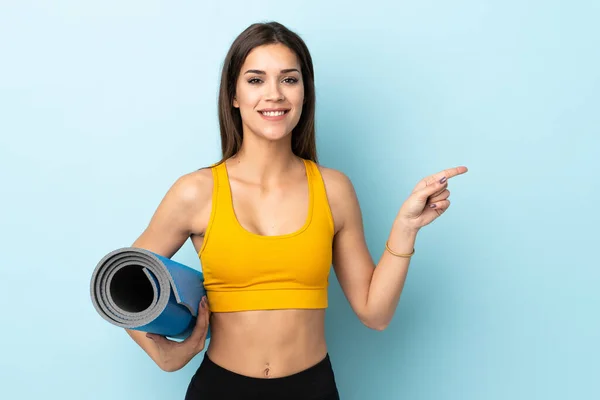 Mujer Joven Deportiva Con Estera Aislada Sobre Fondo Azul Sorprendida — Foto de Stock