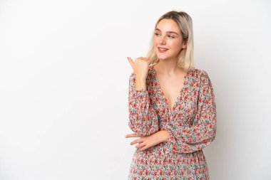 Beyaz arka planda izole edilmiş genç beyaz kadın bir ürünü sunmak için kenarı işaret ediyor.