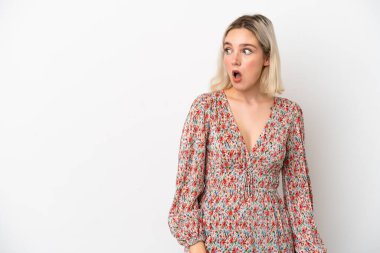 Beyaz arka planda izole edilmiş genç beyaz kadın yan tarafa bakarken sürpriz jest yapıyor.