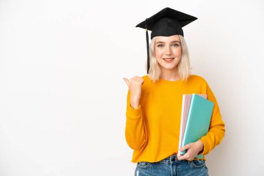 Beyaz arka planda izole edilmiş beyaz bir üniversite mezunu genç bir kadın bir ürün sunmak için kenarı işaret ediyor.