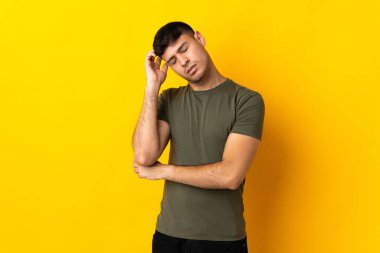 Sarı arka planda başı ağrıyan genç Kolombiyalı bir adam var.