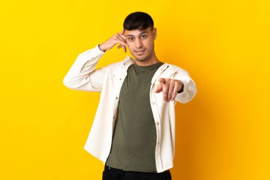 Sarı arka planda izole edilmiş genç Kolombiyalı adam telefon hareketleri yapıyor ve ön tarafı işaret ediyor.