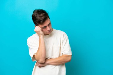 Genç ve yakışıklı Brezilyalı bir adam mavi arka planda soyutlanmış, yorgun ve sıkılmış bir ifadeyle.