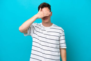 Genç ve yakışıklı Brezilyalı bir adam mavi arka planda tek başına gözlerini elleriyle kapatıyor. Bir şey görmek istemiyorum.