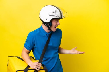 Termal sırt çantalı genç Brezilyalı adam, sarı arkaplanda yalıtılmış ve sürpriz bir ifadeyle yan tarafa bakıyor.