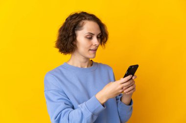 Pembe arka planda izole edilmiş genç bir İngiliz kadın cep telefonuyla mesaj ya da e-posta gönderiyor.
