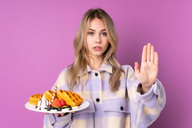 Mor arka planda izole edilmiş waffle 'lar tutan genç Rus kız durdurma hareketi yapıyor ve hayal kırıklığına uğruyor.