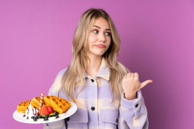 Mor arka planda izole edilmiş waffle 'ları tutan genç Rus kız mutsuzdu ve yan tarafı gösteriyordu.