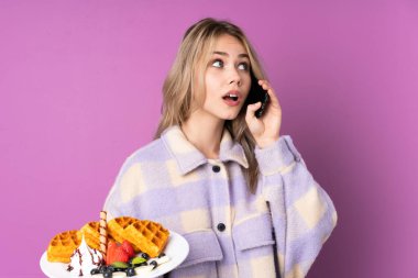 Elinde mor arka planda waffle tutan genç bir Rus kız. Elinde kahve ve cep telefonu var.