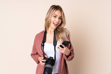 İzole edilmiş arka planda genç fotoğrafçı kız ve telefon zafer pozisyonunda.