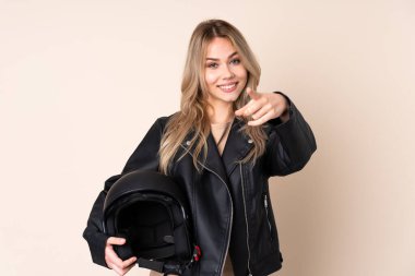 Motosiklet kasklı bir Rus kız, bej arka planda izole edilmiş, telefon hareketleriyle ön tarafı işaret ediyor.