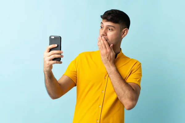 Mladý Kolumbijský Muž Pomocí Mobilního Telefonu Izolované Modré Pozadí Překvapením — Stock fotografie