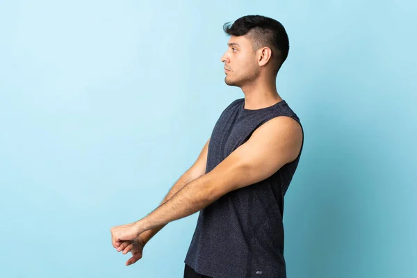 青い背景のストレッチ腕に隔離された若いコロンビア人男性 — ストック写真