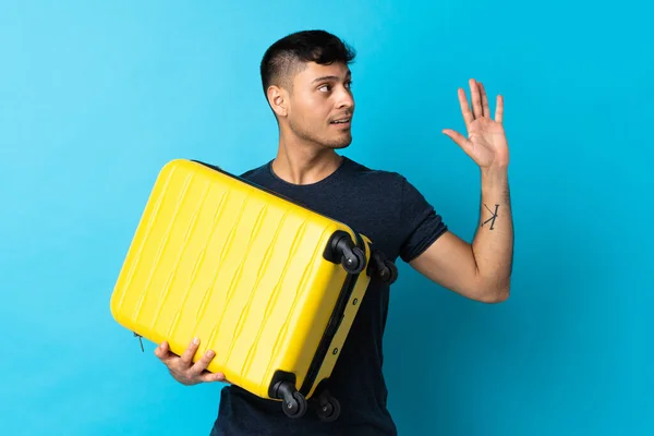 Mladý Kolumbijský Muž Izolovaný Modrém Pozadí Dovolené Cestovním Kufříkem Salutováním — Stock fotografie