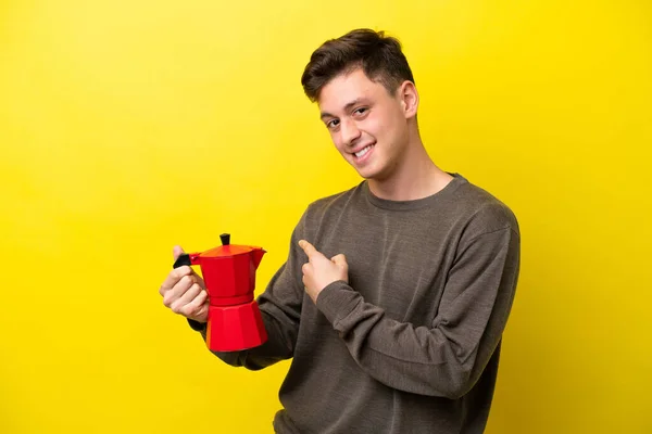 年轻的巴西人拿着用黄色背景隔开的咖啡壶 指着后面 — 图库照片