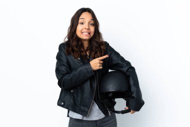 İzole edilmiş beyaz arka plan üzerinde motosiklet kaskı tutan genç bir kadın korkmuş ve kenarı işaret ediyor.