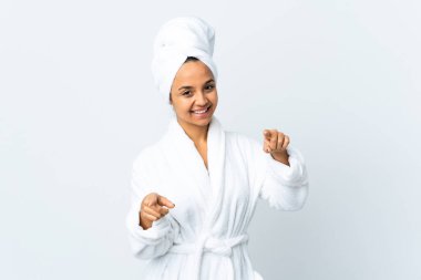 Bornozlu genç kadın izole edilmiş beyaz arka plan üzerinde mutlu bir ifadeyle ön tarafı işaret ediyor.