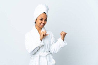 İzole edilmiş beyaz arka planda bornozlu genç bir kadın bir ürün sunmak için kenarı işaret ediyor.