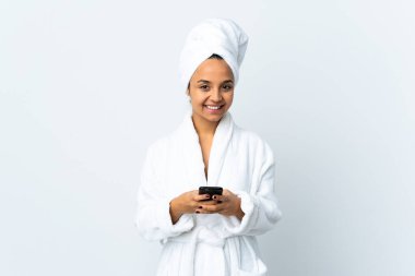 Bornozlu genç kadın izole edilmiş beyaz arka planda cep telefonuyla bir mesaj gönderiyor.