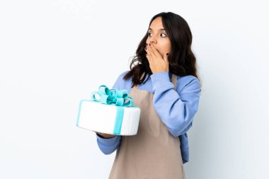 Pasta şefi, beyaz arka planda büyük bir pasta tutuyor. Yan tarafa bakarken sürpriz jest yapıyor.