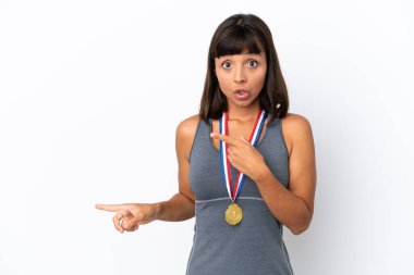 Young mixed race woman with medals isolated on white background surprised and pointing side