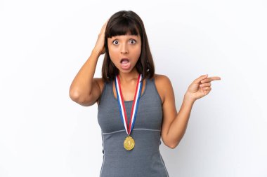 Young mixed race woman with medals isolated on white background surprised and pointing finger to the side