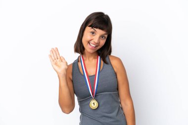 Young mixed race woman with medals isolated on white background saluting with hand with happy expression