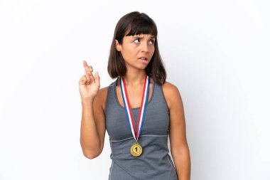Young mixed race woman with medals isolated on white background with fingers crossing and wishing the best